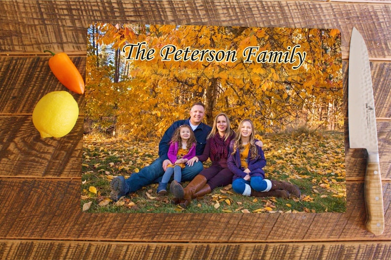 May include: A family of four poses in front of a tree with yellow leaves. The parents are sitting on the ground with their two daughters. The parents are wearing casual clothing and the daughters are wearing dresses. The text "The Peterson Family" is written at the top of the image.