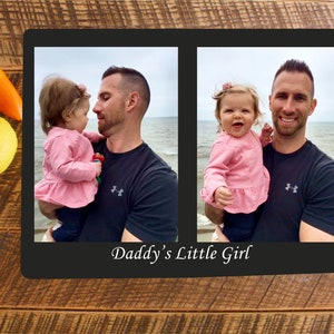 May include: A black framed photo collage with two images of a father holding a young girl. The images are set against a beach background. The text "Daddy's Little Girl" is printed below the images.