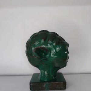 May include: A green Yoda head figurine on a brown base. The figurine is made of plastic and has a detailed face.