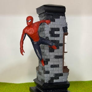 Op de afbeelding: Een beeldje van Spider-Man in een dynamische pose, zich vastklampend aan een bakstenen structuur. De figuur draagt een rood en zwart pak, met een gedetailleerd masker. Het metselwerk is grijs en zwart, en de basis is zwart.