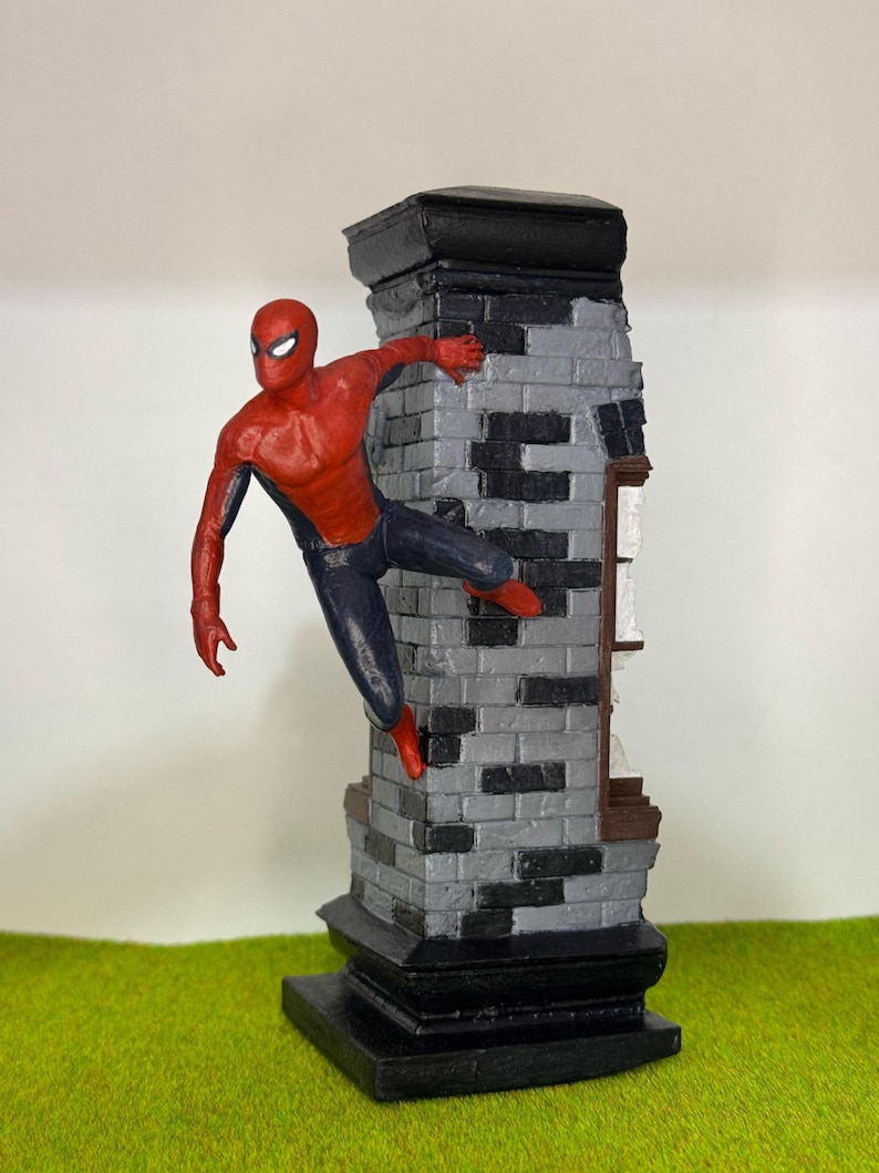 Op de afbeelding: Een beeldje van Spider-Man in een dynamische pose, zich vastklampend aan een bakstenen structuur. De figuur draagt een rood en zwart pak, met een gedetailleerd masker. Het metselwerk is grijs en zwart, en de basis is zwart.