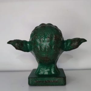 May include: Green Yoda figurine with a distressed paint finish. The figurine is on a base with the words "soulDesign" printed on it.