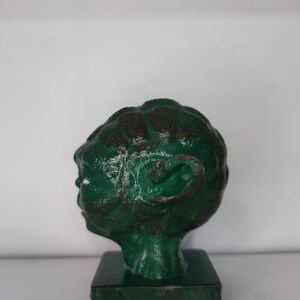 May include: A green 3D printed bust of Yoda from Star Wars. The bust is on a square base and is painted in a distressed green color.