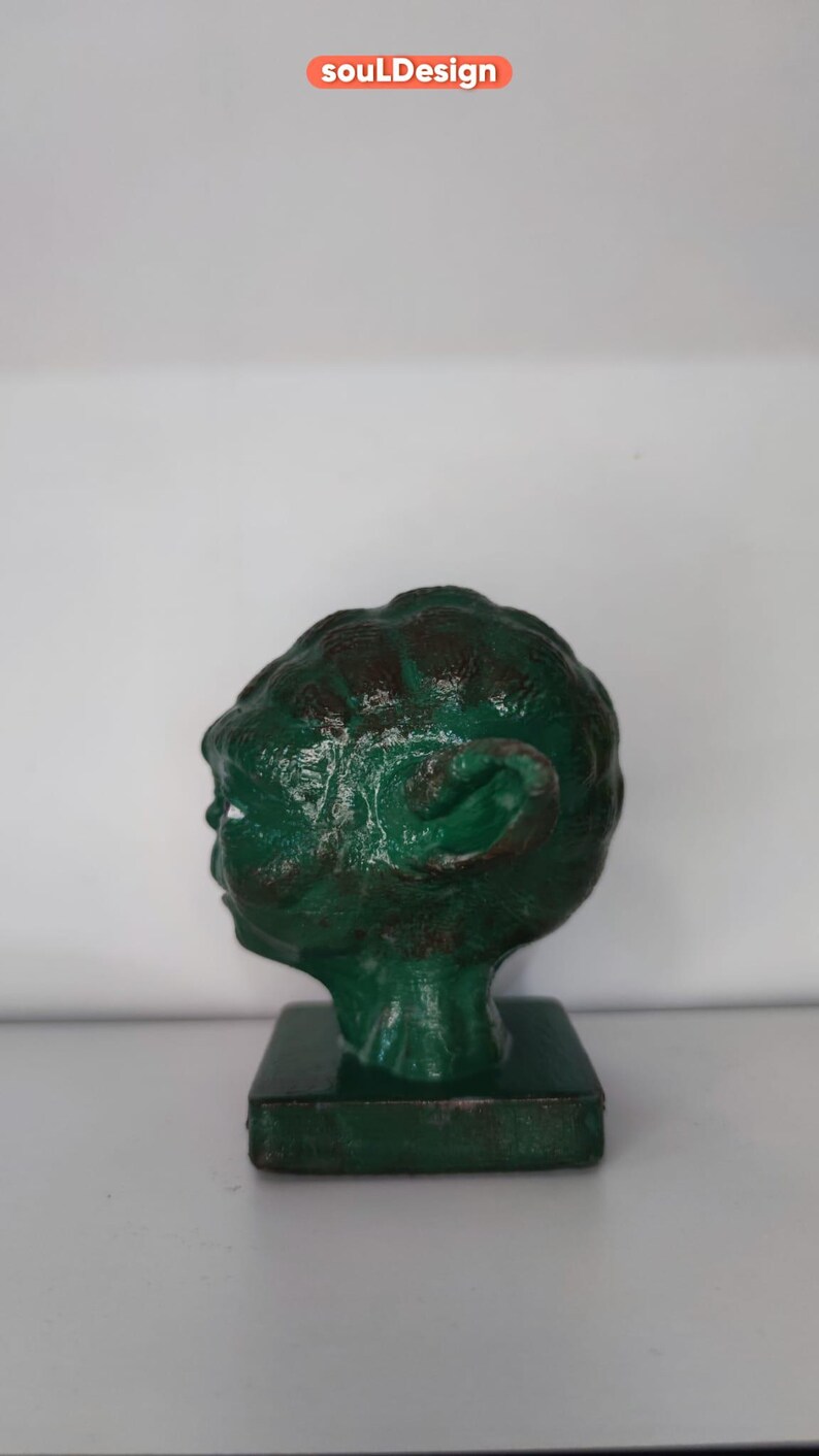 May include: A green 3D printed bust of Yoda from Star Wars. The bust is on a square base and is painted in a distressed green color.