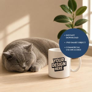 May include: A white ceramic mug with a handle featuring the black text YOUR DESIGN HERE. A dark blue circular overlay displays the white text INSTANT DOWNLOAD, PSD SMART OBJECT, and COMMERCIAL USE INCLUDED. A grey cat is sleeping nearby.