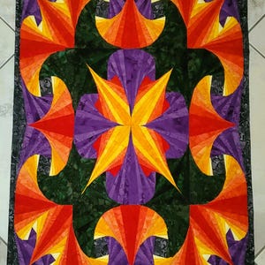 Könnte beinhalten: Eine handgefertigte Steppdecke mit einem lebendigen, geometrischen Design. Die Steppdecke zeigt ein zentrales Sternmuster in Gelb, Orange und Lila, umgeben von sich wiederholenden fächerartigen Formen in ähnlichen Farben. Der Hintergrund ist ein dunkles Grün mit einem gemusterten Rand.