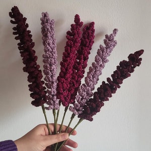 May include: A bouquet of six crocheted lavender stems in shades of burgundy, mauve, and purple.