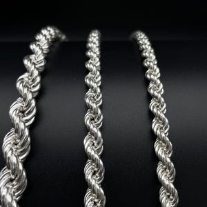May include: Three silver rope chains of varying lengths, displayed against a black background.