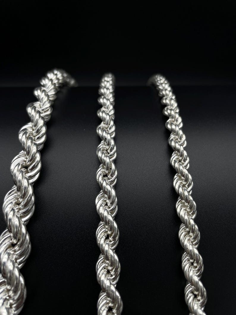 May include: Three silver rope chains of varying lengths, displayed against a black background.