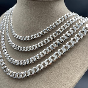 May include: A display of silver curb chain necklaces in varying thicknesses. The necklaces are draped over a mannequin bust, showcasing the different sizes and the reflective quality of the metal. The chains are a bright, polished silver.