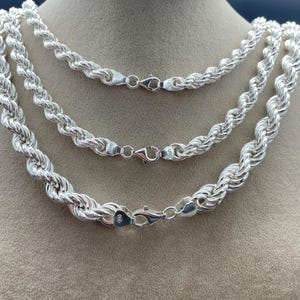 May include: Three silver rope chains of different lengths, displayed on a brown surface. The chains are made of a twisted rope design and have lobster claw clasps.