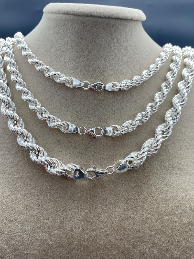 May include: Three silver rope chains of different lengths, displayed on a brown surface. The chains are made of a twisted rope design and have lobster claw clasps.