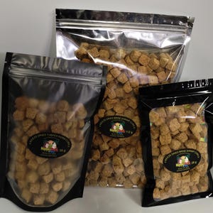 May include: Three sealed bags of freeze-dried fish food cubes. The bags are various sizes, with the largest bag in a silver pouch and the other two in black pouches. The labels read "Freeze Dried Tubifex Worm Cubes" and "Freeze Dried Brine Shrimp Cubes".