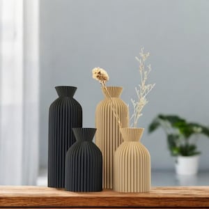 以下が含まれることがあります： 黒とベージュのプリーツデザインの装飾的な花瓶が4つ。花瓶は木製の表面に一列に並んでいます。