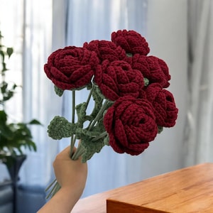 Könnte beinhalten: Ein Strauß aus sieben gehäkelten roten Rosen mit grünen Blättern und Stielen.