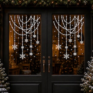 May include: White snowflake and beaded garland window decals applied to a set of black double doors. The design features multiple draped strings of beads with hanging snowflake ornaments of varying sizes, creating a festive winter decoration.
