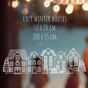 May include: A white line art decal featuring a row of five winter houses and two pine trees. The text reads COZY WINTER HOUSES, 60 x 20 CM, and 100 x 35 CM. The design includes details like wreaths, stars, and windows on the house facades.