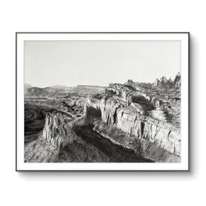 May include: A black and white photograph of a rocky landscape with a canyon in the foreground. The canyon is carved into the rock and the rock formations are layered and textured. The sky is clear and the sun is shining.