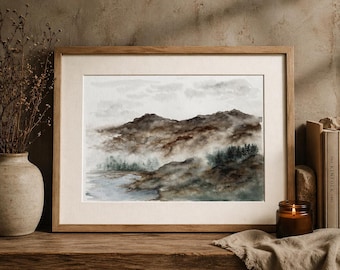 May include: Watercolor landscape art print featuring a mountain range in shades of brown and gray, with a misty atmosphere. The artwork is framed in a light wood frame and matted with a cream-colored mat.