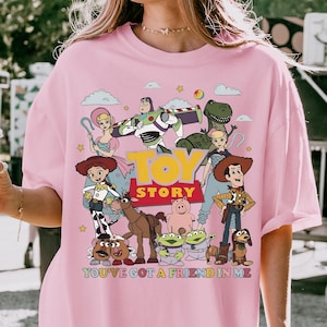 Może przedstawiać: R&oacute;żowa, obszerna koszulka z kolorową grafiką postaci z filmu "Toy Story". Projekt zawiera napisy "TOY STORY" i "YOU'VE GOT A FRIEND IN ME". Swobodny, wygodny styl.