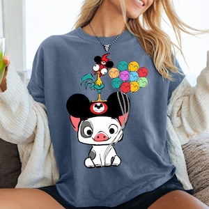 K&ouml;nnte beinhalten: Blaues T-Shirt mit einem Cartoon-Schwein, das einen Mickey-Mouse-Hut tr&auml;gt, mit einem Hahn und bunten Luftballons. Das Shirt hat eine lockere Passform und kurze &Auml;rmel.