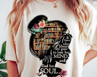 May include: A white t-shirt with a graphic of a woman standing in a library with bookshelves filled with books. The text on the shirt reads "& Into the library she goes to lose her MIND and find her SOUL."