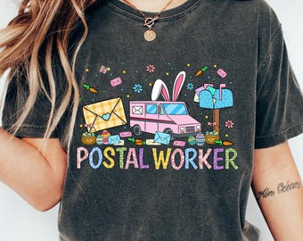 May include: Dark gray t-shirt with a colorful "Postal Worker" graphic. The design features a pink mail truck with bunny ears, envelopes, and Easter eggs. The shirt is a comfortable, casual style.