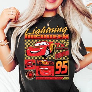 May include: Black t-shirt featuring Lightning McQueen from the Cars film. The design includes the text "Lightning McQueen" in yellow and red, along with images of the character and the number "95".