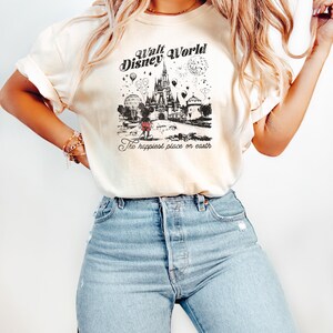 Puede incluir: Camiseta color crema con un gr&aacute;fico en blanco y negro del castillo de Cenicienta, globos y el texto "Walt Disney World" y "The happiest place on earth." La camiseta se combina con vaqueros azul claro.