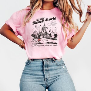 Puede incluir: Camiseta rosa claro con un gr&aacute;fico en blanco y negro del castillo de Walt Disney World, Mickey Mouse y otros elementos del parque. Tambi&eacute;n se muestra el texto "Walt Disney World" y "The happiest place on earth".