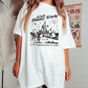 Puede incluir: Camiseta blanca con un gr&aacute;fico en blanco y negro del castillo de Cenicienta, Mickey Mouse y el texto "Walt Disney World" y "The happiest place on earth". La camiseta tiene mangas cortas y un corte holgado.
