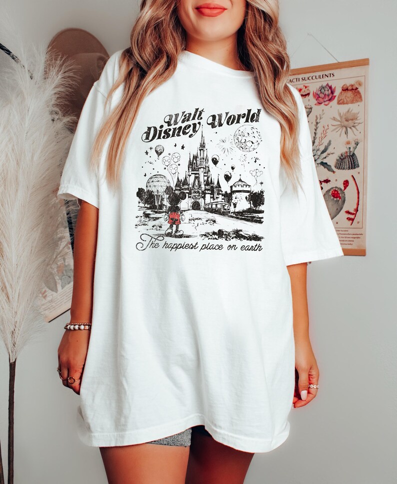 Puede incluir: Camiseta blanca con un gr&aacute;fico en blanco y negro del castillo de Cenicienta, Mickey Mouse y el texto "Walt Disney World" y "The happiest place on earth". La camiseta tiene mangas cortas y un corte holgado.