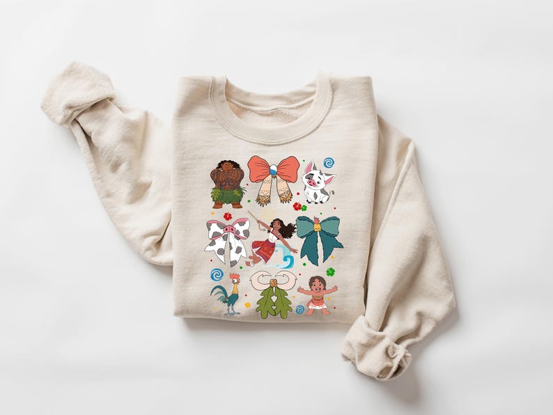 May include: A beige sweatshirt featuring colorful cartoon characters and bows. The design includes a rooster, a pig, and a girl with a bow. The sweatshirt is made of a soft material and has a crew neck.