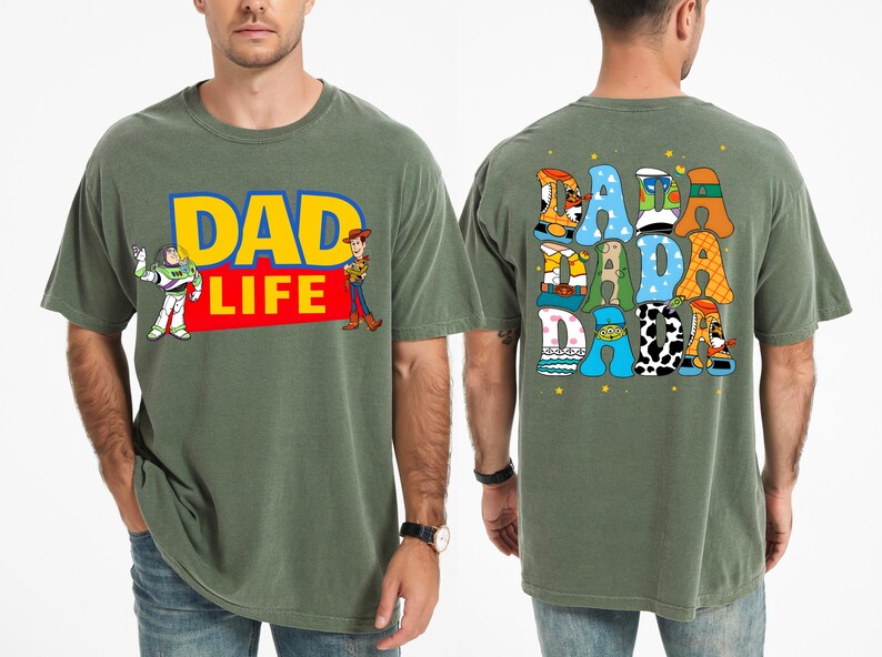 K&ouml;nnte beinhalten: Olivgr&uuml;nes T-Shirt mit dem Text "DAD LIFE" in Gelb und Rot, mit den Zeichentrickfiguren Buzz Lightyear und Woody. Auf der R&uuml;ckseite des Shirts steht "DADA DADA DADA" in einer farbenfrohen, verspielten Schrift.