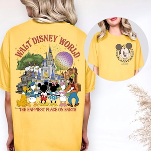 May include: Yellow t-shirt featuring a graphic of Disney characters and the text "WALT DISNEY WORLD" and "THE HAPPIEST PLACE ON EARTH". The design includes Mickey Mouse, Minnie Mouse, Donald Duck, Daisy Duck, Goofy, and a train.