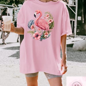 Pu&ograve; includere: T-shirt rosa chiaro con un motivo di fenicottero. Il fenicottero &egrave; rosa con un becco nero, circondato da fiori e foglie tropicali. La maglietta &egrave; rosa chiaro e ha maniche corte.
