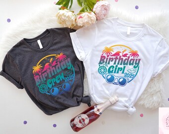 May include: Two t-shirts, one charcoal and one white, with colorful graphic designs. The designs feature the text "Birthday Crew 2025" and "Birthday Girl 2025" in a tropical theme with sunglasses and palm trees.