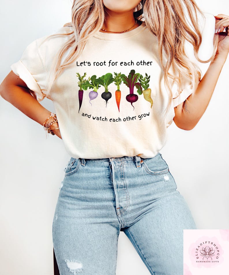Może przedstawiać: Biała koszulka z napisem "Let's root for each other and watch each other grow" i grafiką kolorowych warzyw.