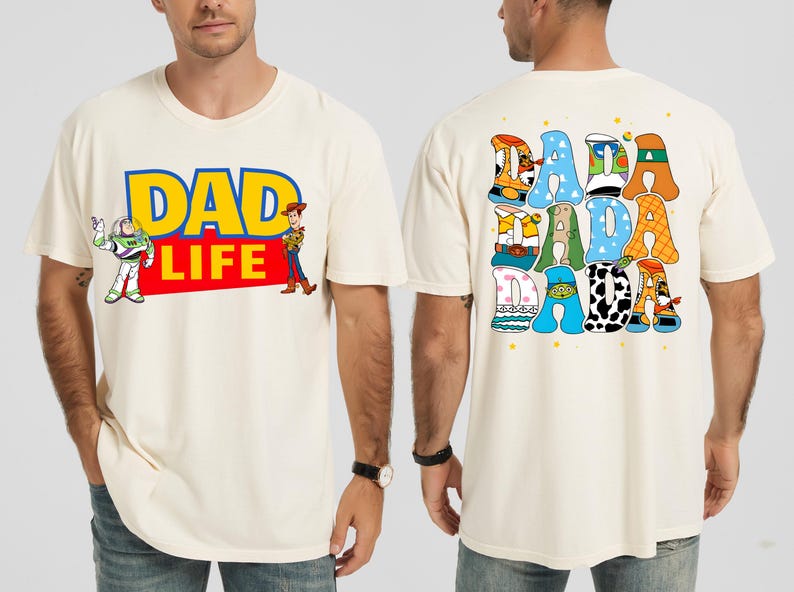K&ouml;nnte beinhalten: Cremefarbenes T-Shirt mit dem Text "DAD LIFE" in Blau und Gelb, mit Illustrationen von Buzz Lightyear und Woody. Auf der R&uuml;ckseite des Shirts steht "DADA" in bunten, gemusterten Buchstaben. Ein l&auml;ssiges, lustiges Design.