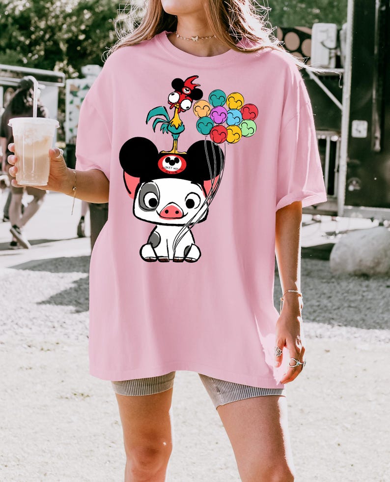 K&ouml;nnte beinhalten: Hellrosa T-Shirt mit einer Cartoon-Schwein-Figur mit Mickey Mouse-Ohren, die bunte Luftballons h&auml;lt. Ein Cartoon-Hahn sitzt auf dem Kopf des Schweins. Das T-Shirt hat eine lockere Passform.