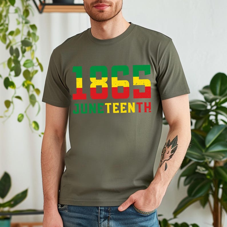 May include: An olive green t-shirt featuring the text "1865 Juneteenth" in green, yellow, and red. The t-shirt has a crew neck and short sleeves. The design is a bold, colourful statement.