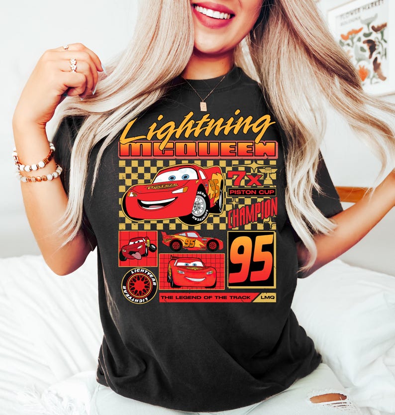 May include: Black t-shirt featuring Lightning McQueen from the Cars film. The design includes the text "Lightning McQueen" in yellow and red, along with images of the character and the number "95".