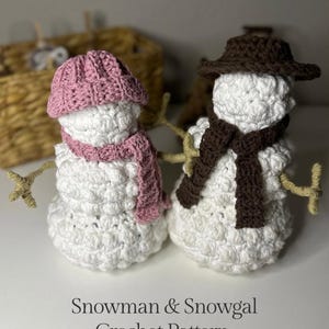 May include: A crochet pattern for a snowman and snowgal. The pattern is for a weighted set. The snowman is wearing a brown hat and a brown scarf. The snowgal is wearing a pink hat and a pink scarf.