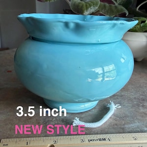 May include: A glossy light blue ceramic self-watering planter with a ruffled rim and a rounded body. The text 3.5 inch NEW STYLE is visible. A white cotton wick lies in front of the planter next to a ruler showing 3.5 inches.