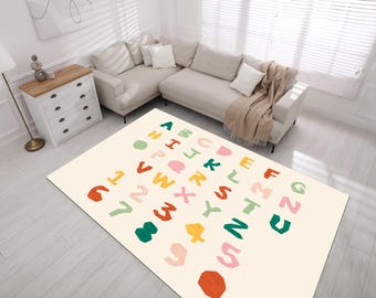 May include: A rectangular cream-colored rug with colorful letters and numbers. The letters A through Z and the numbers 1 through 5 are displayed in a playful, cut-out style. The rug is placed in a living room setting with a beige sectional sofa.