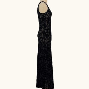 K&ouml;nnte beinhalten: Ein schwarzes, bodenlanges Kleid mit floralem Muster. Das &auml;rmellose Kleid wird auf einer Schaufensterpuppe pr&auml;sentiert. Der Stoff scheint Samt oder ein &auml;hnliches Material mit dezentem Glanz zu sein. Das Kleid hat einen Rundhalsausschnitt und eine taillierte Silhouette.