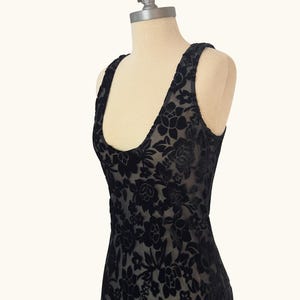 K&ouml;nnte beinhalten: Schwarzes &auml;rmelloses Kleid mit floralem Muster. Das Kleid besteht aus einem transparenten Stoff mit samtartiger Textur und wird auf einer Schaufensterpuppe pr&auml;sentiert. Es hat einen Rundhalsausschnitt und breite Tr&auml;ger.