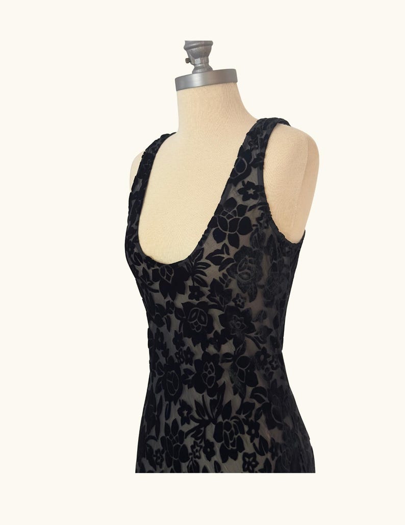 K&ouml;nnte beinhalten: Schwarzes &auml;rmelloses Kleid mit floralem Muster. Das Kleid besteht aus einem transparenten Stoff mit samtartiger Textur und wird auf einer Schaufensterpuppe pr&auml;sentiert. Es hat einen Rundhalsausschnitt und breite Tr&auml;ger.