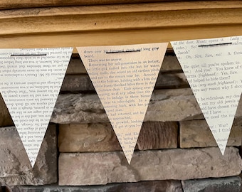 May include: A decorative banner composed of three triangular pennants. Each pennant is crafted from aged book pages, displaying printed text. The banner hangs against a backdrop of a stone wall and wooden trim.