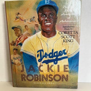 Könnte beinhalten: Buchcover mit einem Porträt von Jackie Robinson in einer Baseballuniform der Dodgers. Das Cover ist überwiegend gelb und blau, mit dem Text "Dodger JACKIE ROBINSON BASEBALL GREAT". Zusätzlicher Text enthält "No. 13 Americans of Achievement" und "Introductory Essay by CORETTA SCOTT KING."